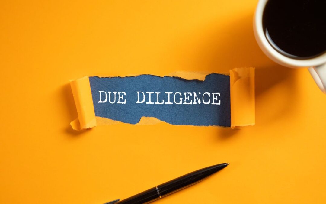 Due diligence: an orange desk with a pen and coffee mug on it, torn like a piece of paper in the centre where the words 'due diligence' are revealed.